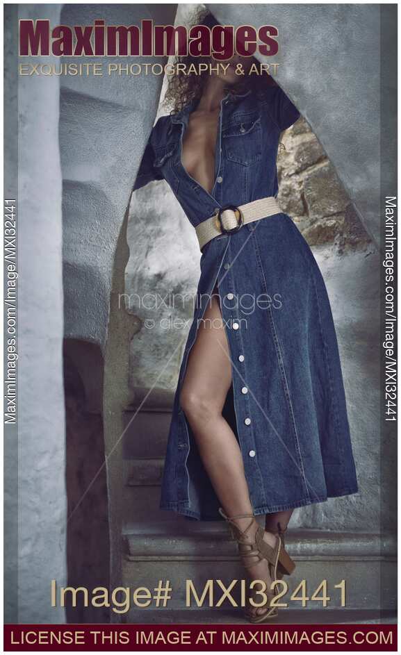 Sexy young woman in unbuttoned denim dress revealing her legs and cleavage standing on a staircase seductive look