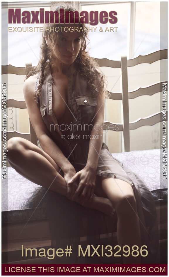 Sexy young woman in unbuttoned dress sitting by an open window in bright soft daylight with expressive look