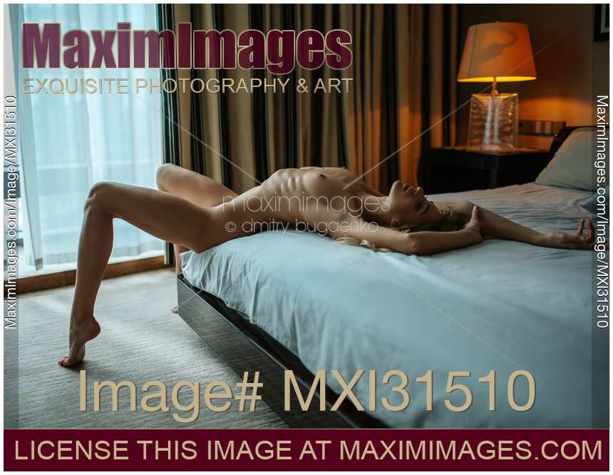 Sexy young woman lying naked on the edge of a bed with her chest arched upwards