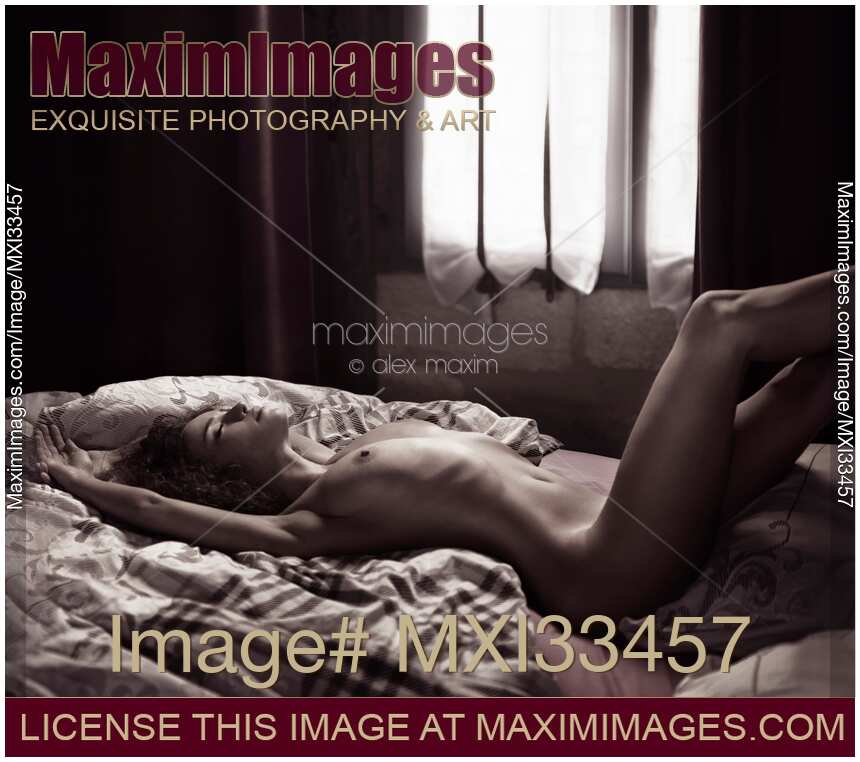Sexy young woman lying naked relaxed on a bed in soft daylight from a window Black and white