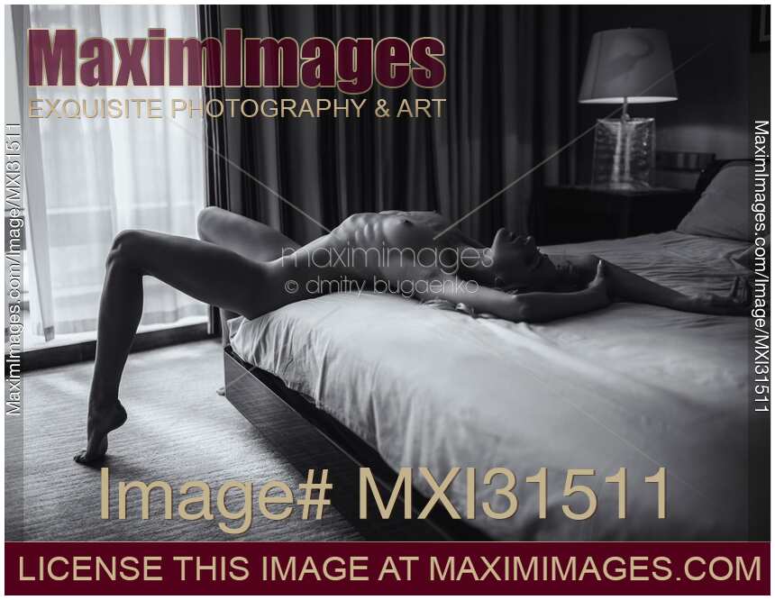 Sexy young woman lying nude on the edge of a bed with her legs apart Black and white