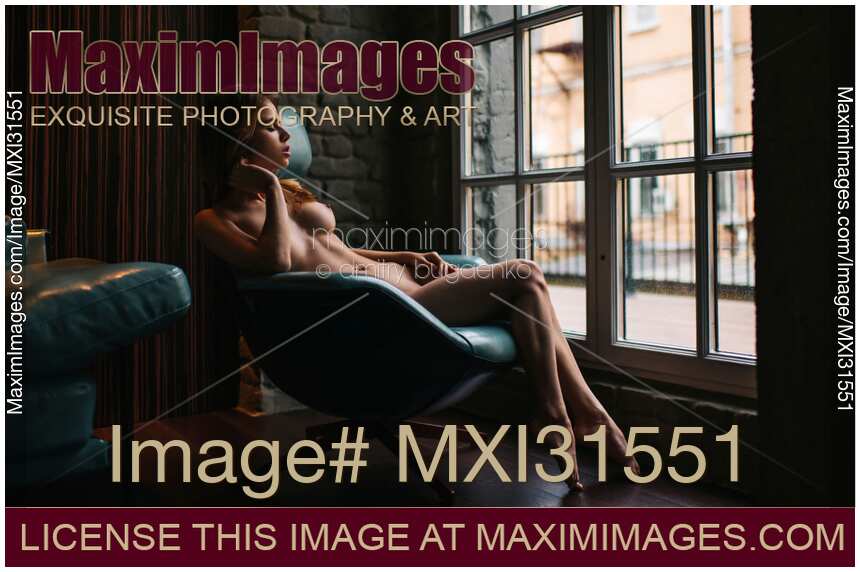 Sexy young woman sitting naked in a chair by the window