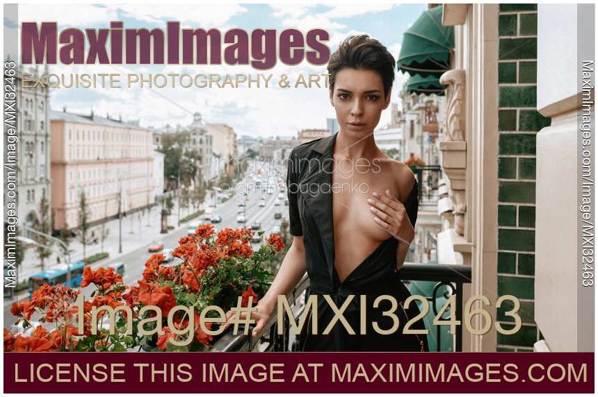 Sexy young woman standing half naked on a balcony covering her breast with a hand