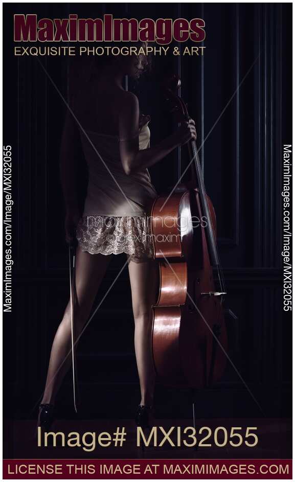 Sexy young woman standing with a cello in dark room with dramatic light falling on her bare legs in high heels