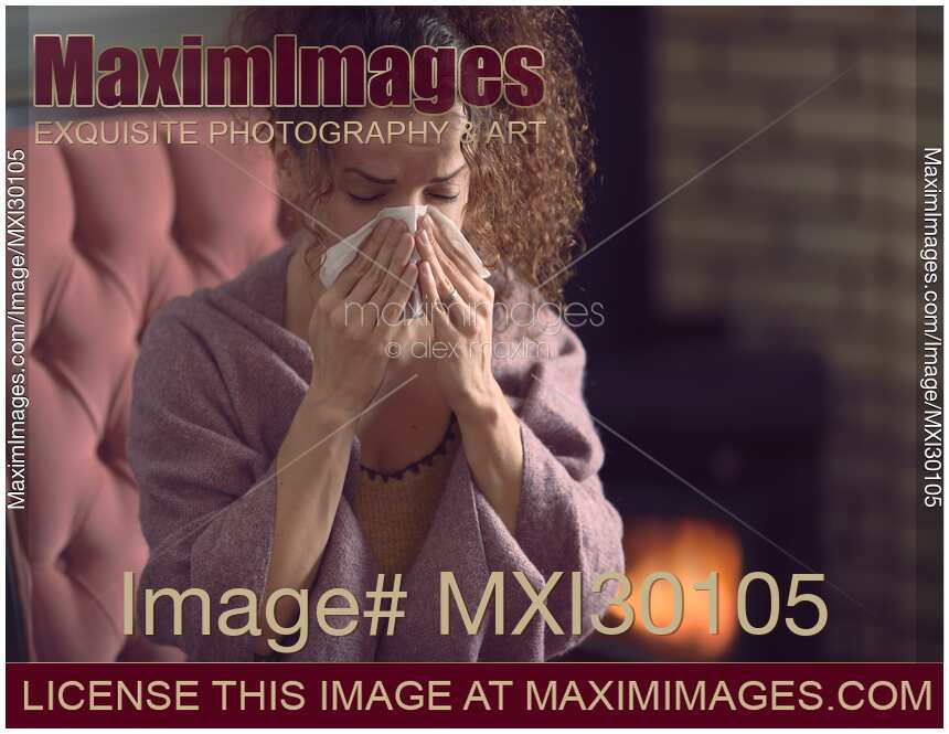 Sick with cold woman blowing her nose in paper tissue at home