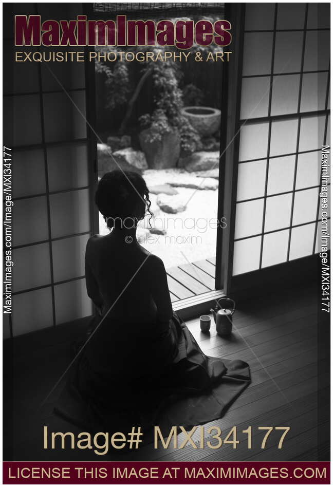 Silhouette of a woman with bared back sitting inside by an open Shoji door looking at Japanese Zen garden. Black and white.