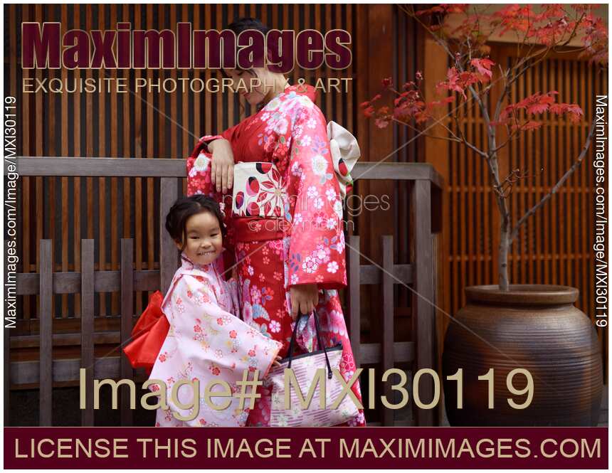 Smiling little girl and her mother dressed in red kimonos on the street in Gion Kyoto Japan