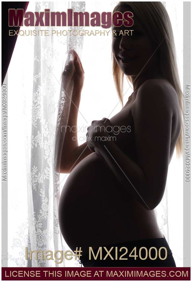 Smiling Pregnant Woman Standing at a Window