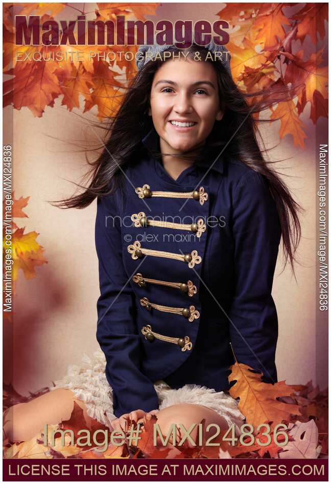 Smiling teenage girl sitting on red autumn leaves