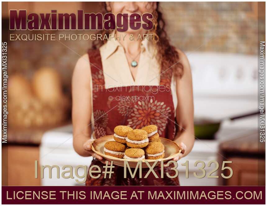Smiling young woman in an apron holding a plate of freshly baked home-made cookies