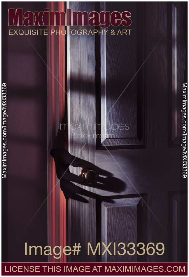 Spooky male hand in a glove reaching for a door handle from behind a door in a dark shadowy room