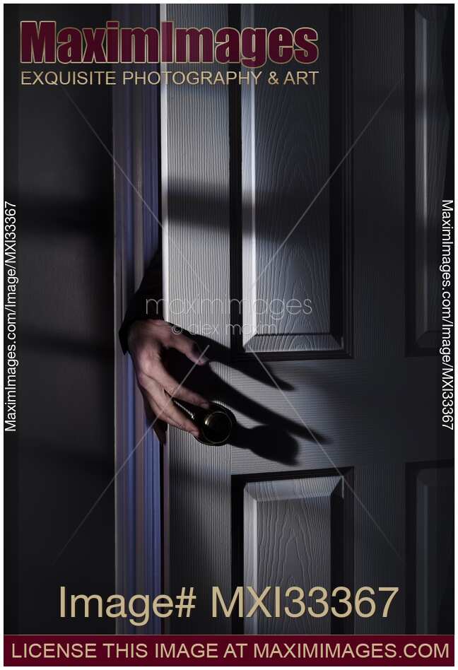 Spooky male hand reaching for a door handle from behind a door in a dark shadowy house room