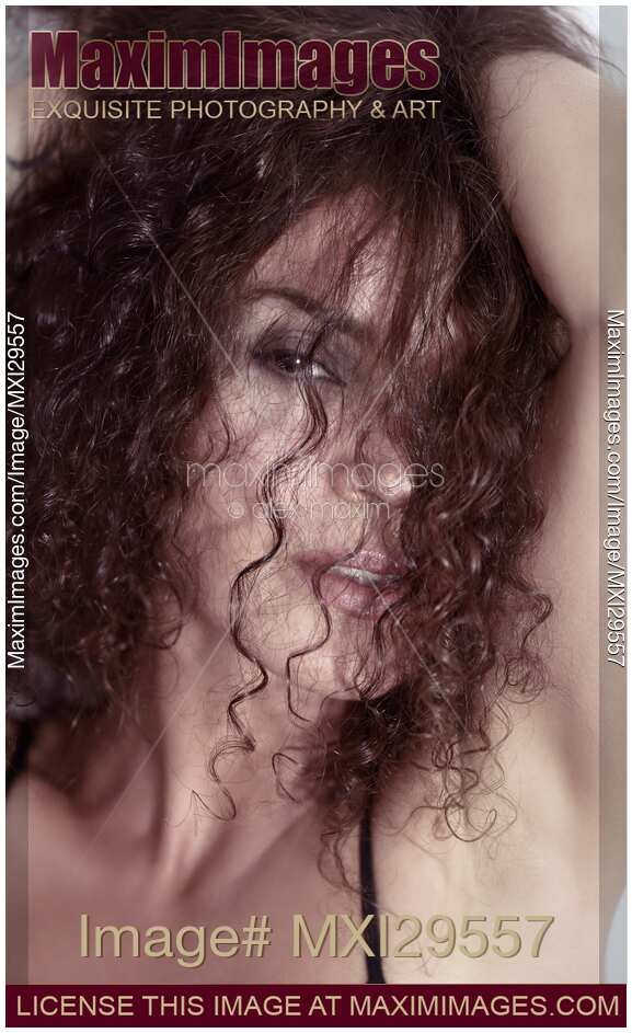 Sultry beauty face portrait of young woman looking through her long curly brown hair
