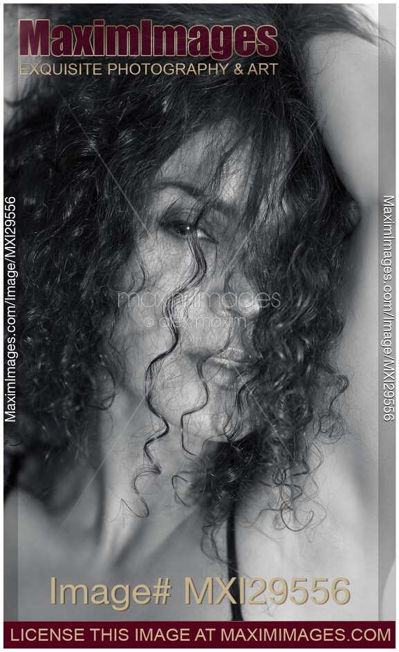 Sultry beauty face portrait of young woman looking through her long curly dark hair Black and white