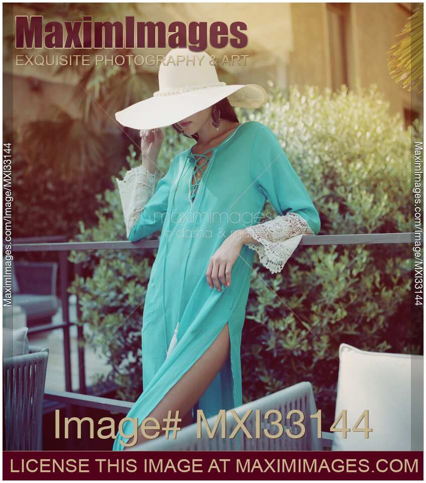Summer fashion lifestyle portrait of an elegant woman in a turquoise sheer beach kaftan dress on a terrace