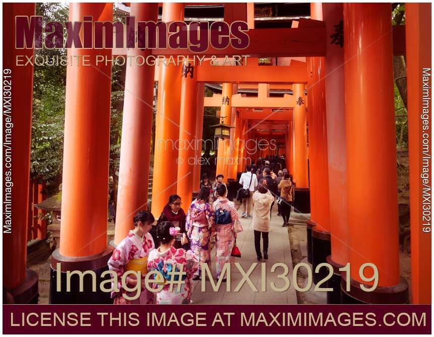 Tourists and women in kimono walking along a long Senbon torii path at Fushimi Inari shrine in Kyoto Japan
