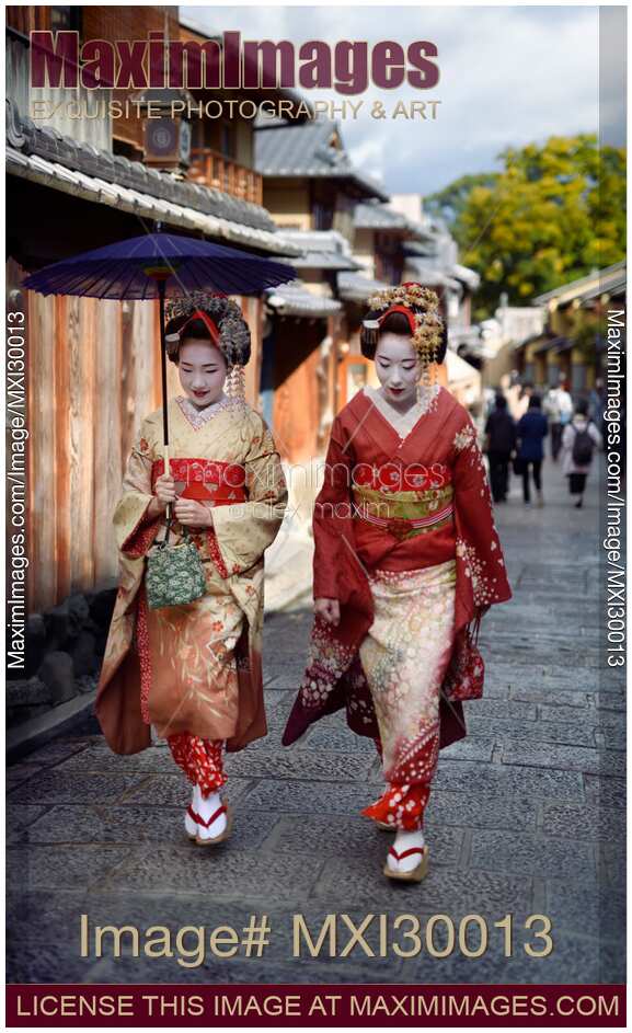Two beautiful Maiko, Geisha apprentices in colorful kimonos walking on an old street in Kyoto