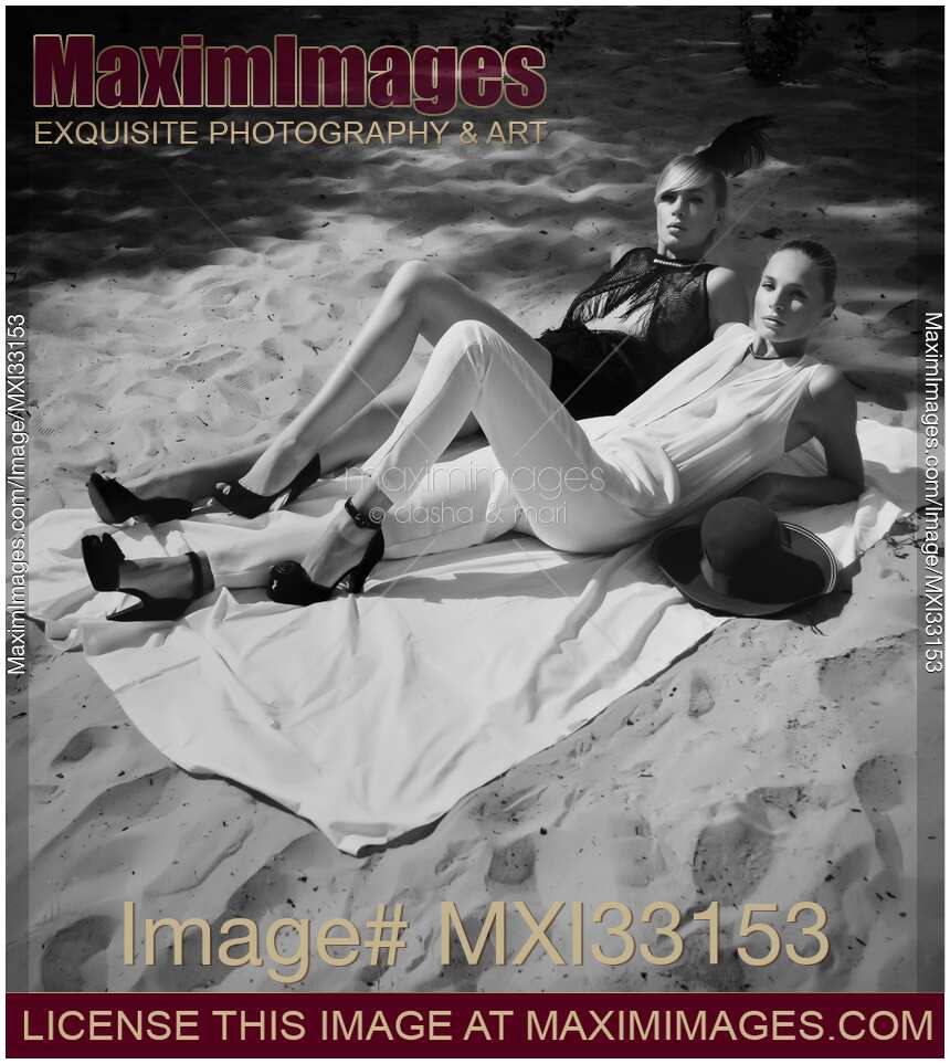 Two fashionably dressed sexy young women lying on the beach wearing high heels