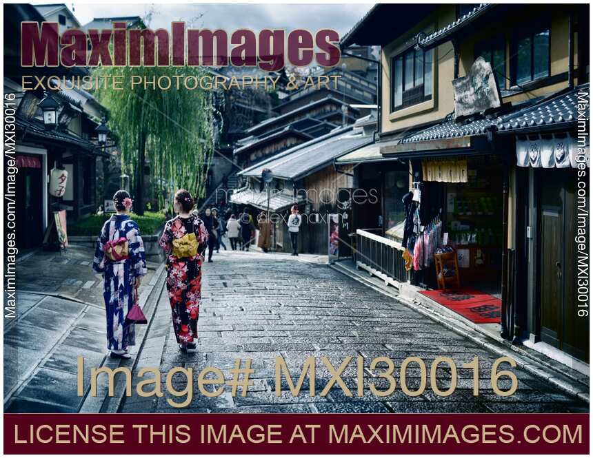 Two girls in bright Yukata kimonos with their obi tied in bow walking on street in Kyoto Japan