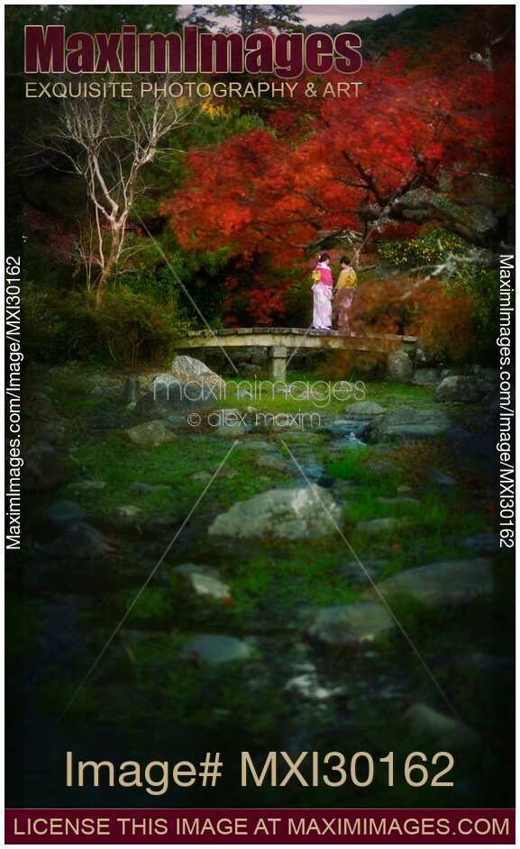 Two girls in kimono standing on a bridge in Japanese garden in autumn