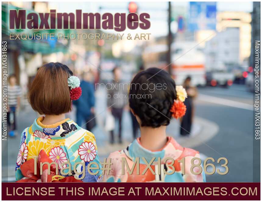 Two Japanese girls in bright Yukatas and colorful flowers in their hair on streets of Kyoto