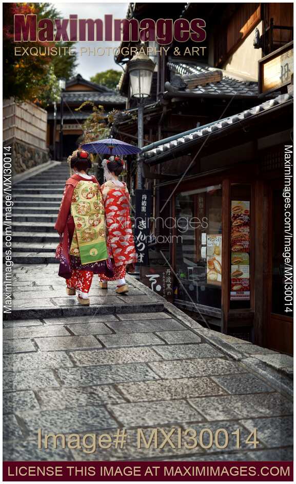 Two Maiko, Geisha apprentices in beautiful colorful kimono with long obi walking on old street in Kyoto Japan