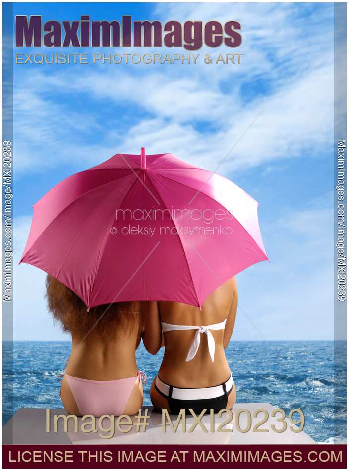 Two women sitting together under umbrella on sea shore