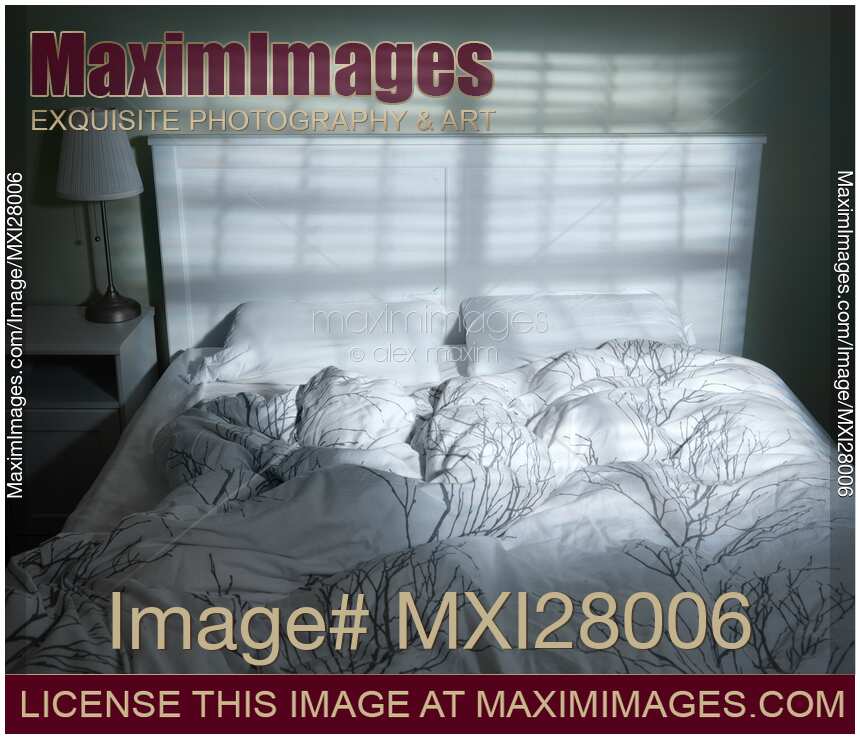 Unmade empty bed with light coming through window blinds