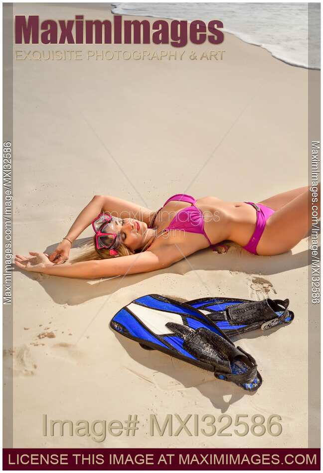 View from above of a sexy woman in pink bikini swimsuit sunbathing lying on sandy beach with goggles and fins
