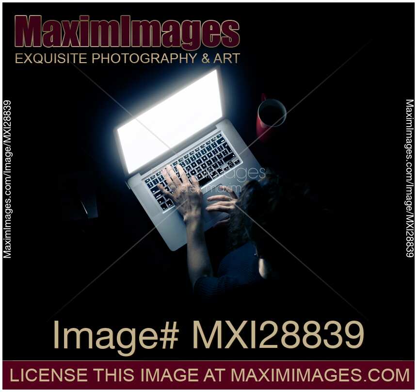 Woman at a desk in darkness with a glowing laptop computer screen