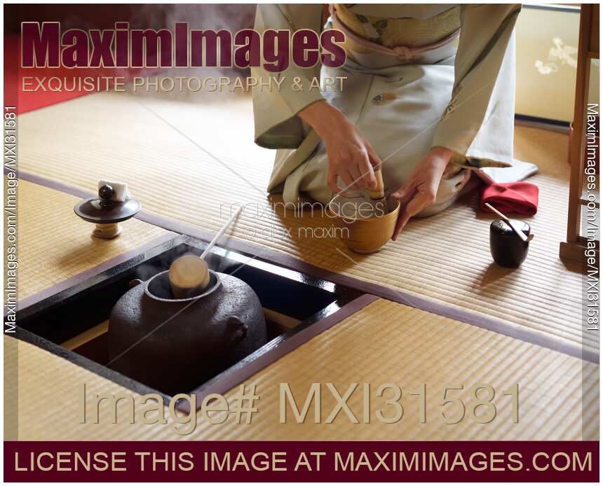 Woman blending matcha tea with a whisk by a steaming iron kettle in a Japanese tea house