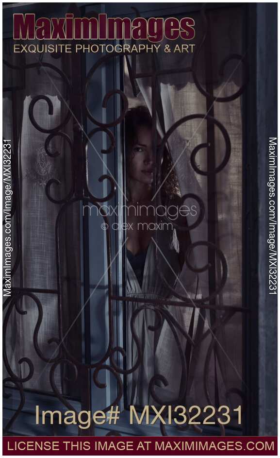 Woman face looking outside through a window behind grates at night
