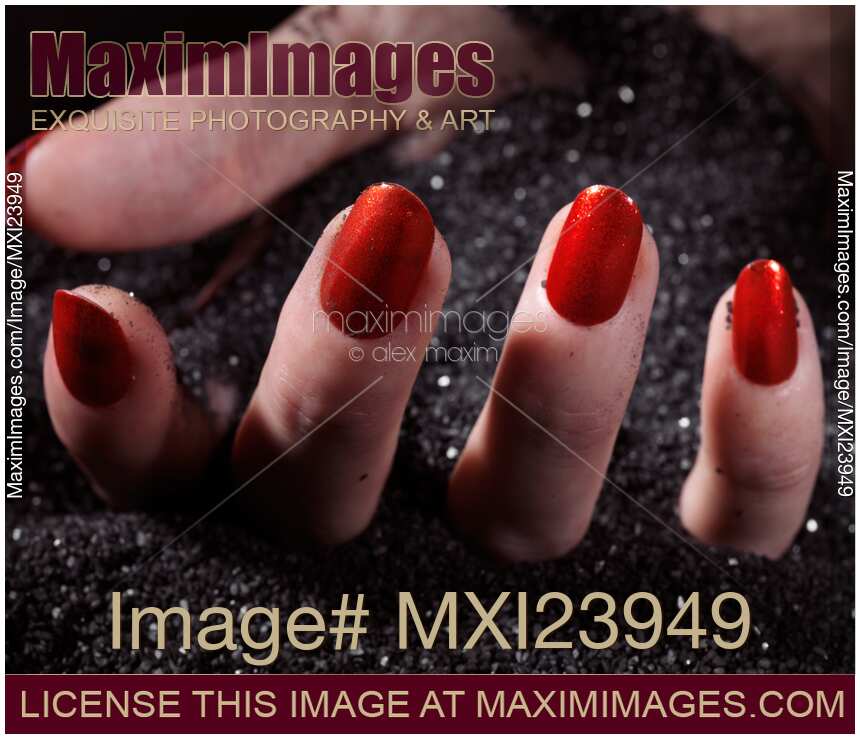 Woman Hand with Red Nail Polish Buried in Black Sand