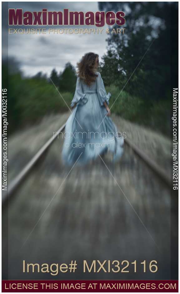 Woman in a long dress walking along railroad tracks in the wind