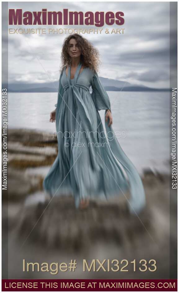 Woman in a long dress walking along the sea shore in a dramatic stormy scenery