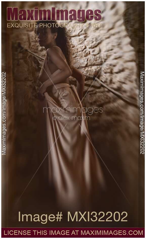Woman in a long gown walking up a dark spiral staircase of a French house looking back