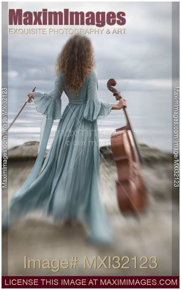 Woman in a long vintage dress standing gracefully by the ocean shore with a cello and a bow