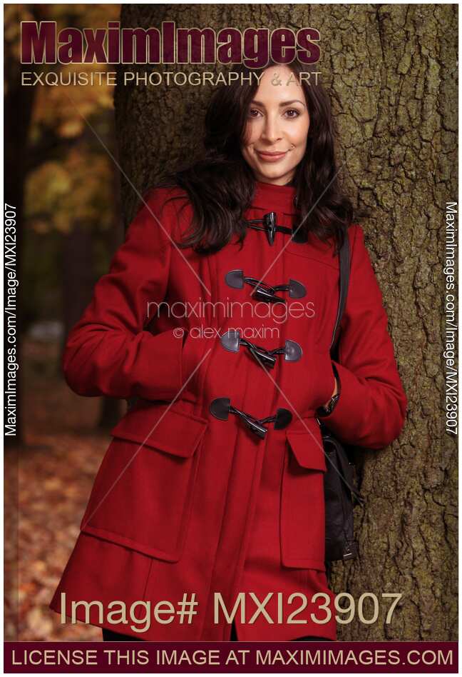 Woman in a Red Coat Leaning Against a Tree in a Park