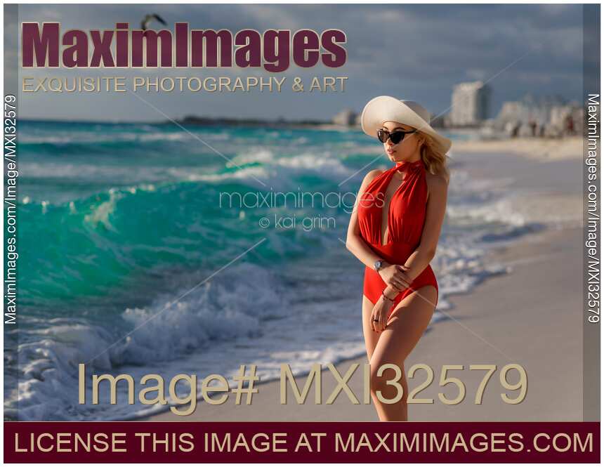 Woman in a red swimsuit sun hat and sunglasses walking along a sandy beach of Caribbean Sea shore in Cancun