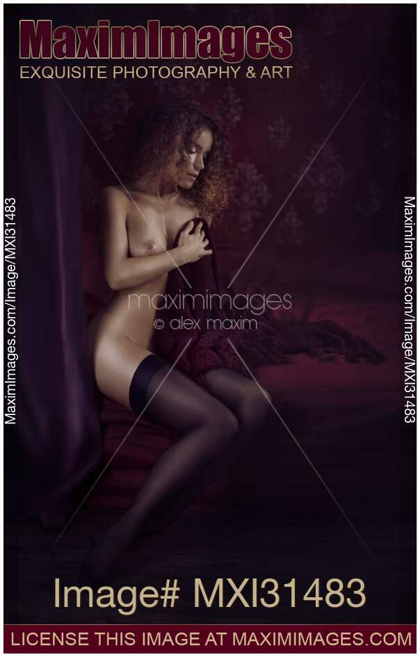 Woman in black stockings sitting naked on bed covering her breast with a blanket