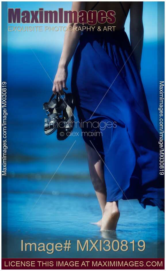 Woman in blue dress walking barefoot on ocean beach sand