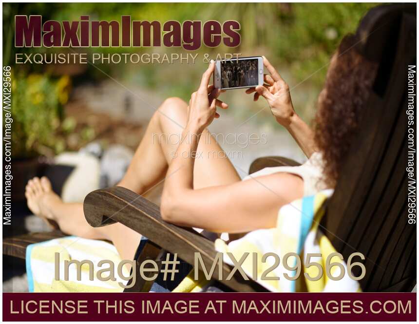 Woman in chaise lounge sunbathing with an iPhone in her hands