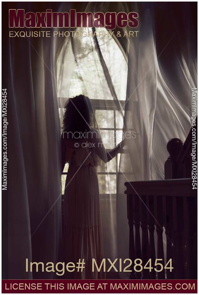 Woman in dress standing by the window in dark house