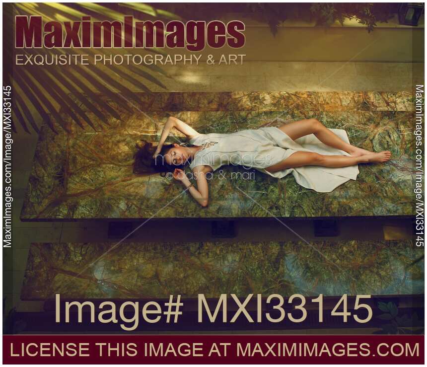 Woman in elegant dress lying on stone table on summer terrace in a sensual pose. View from above.