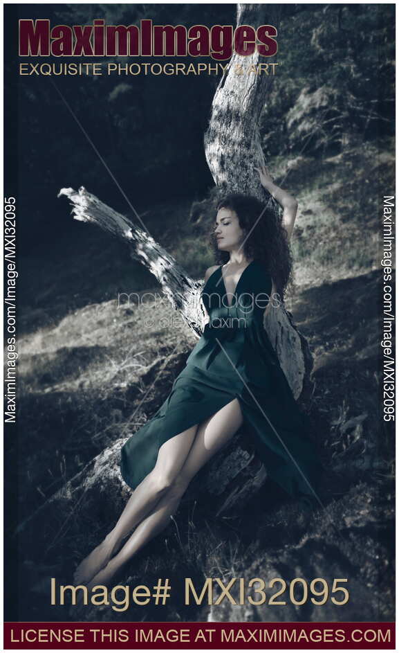 Woman in green dress lying on a dried tree with a dreamy relaxed expression