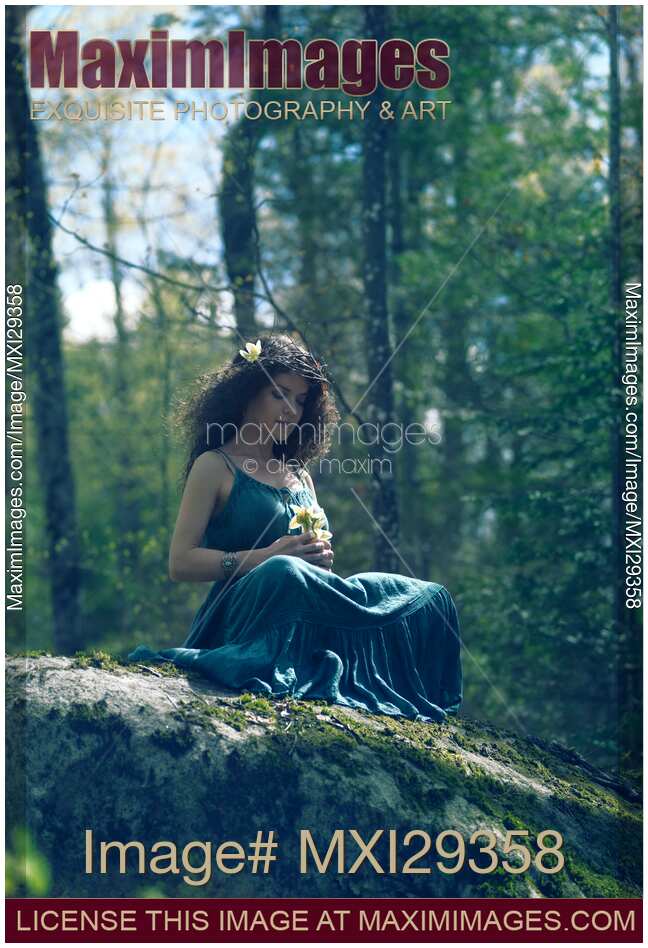 Woman in green dress sitting on rocks in the nature with a flower in her hands