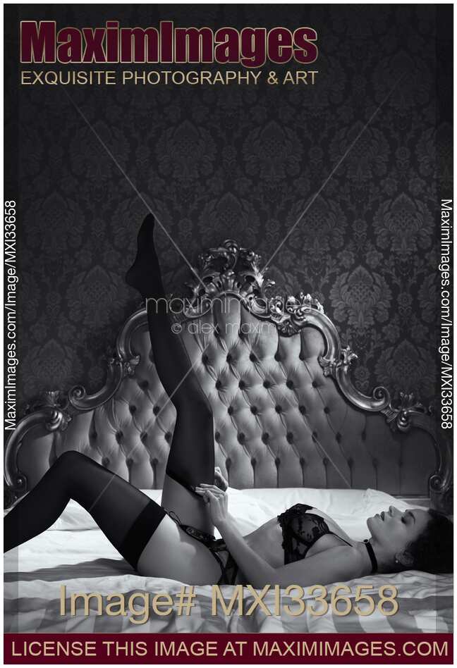 Woman in lingerie putting on black stockings on her sexy legs lying on antique bed in vintage bedroom Black and white