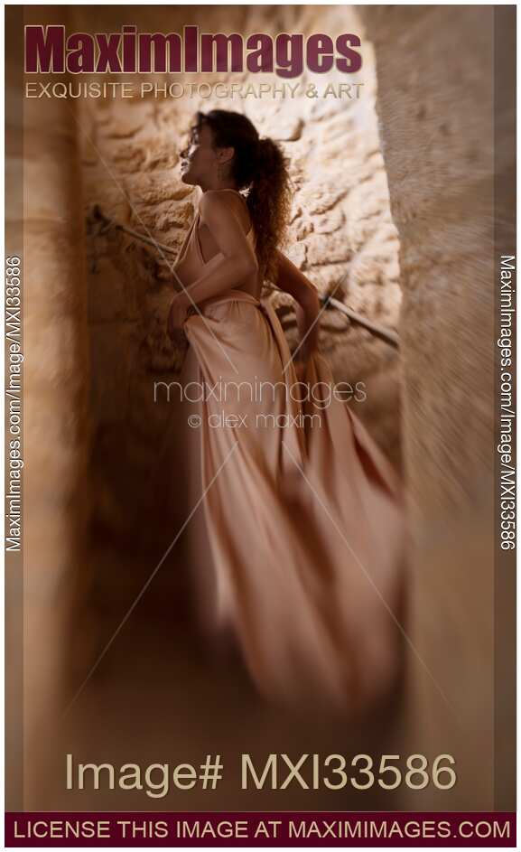 Woman in long dress running up the stairs of a spiral staircase in a dungeon of a medieval stone castle
