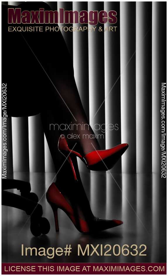 Woman in office with legs in black stockings and sexy red high-heel shoes