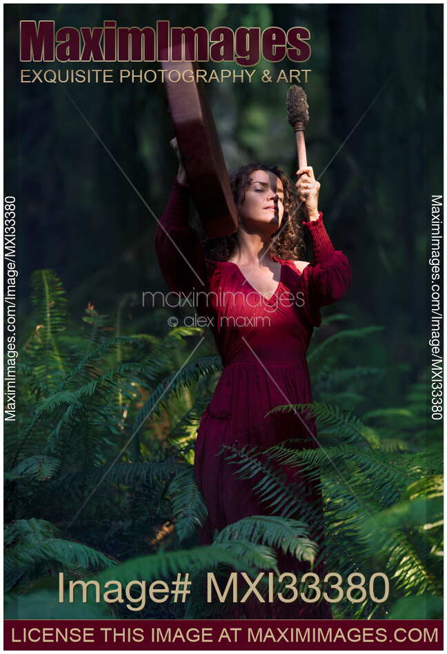 Woman in red dress beating shamanic drum in tranquil dark forest nature scenery
